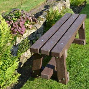 TDP 1.5m Trail bench made from recycled plastic. Shown on grass in front of a stone wall