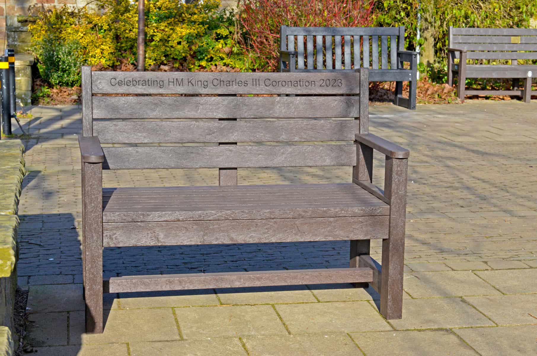 King Charles III coronation commemorative two seater bench with Engraving. Made from recycled plastic TDP Wirksworth 1.2m in brown with a black dale in the background