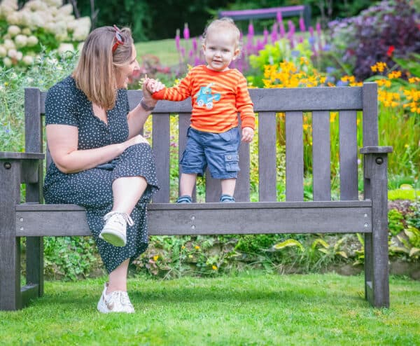TDP Recycled Three seater Dale bench in brown in a garden setting with mother and child